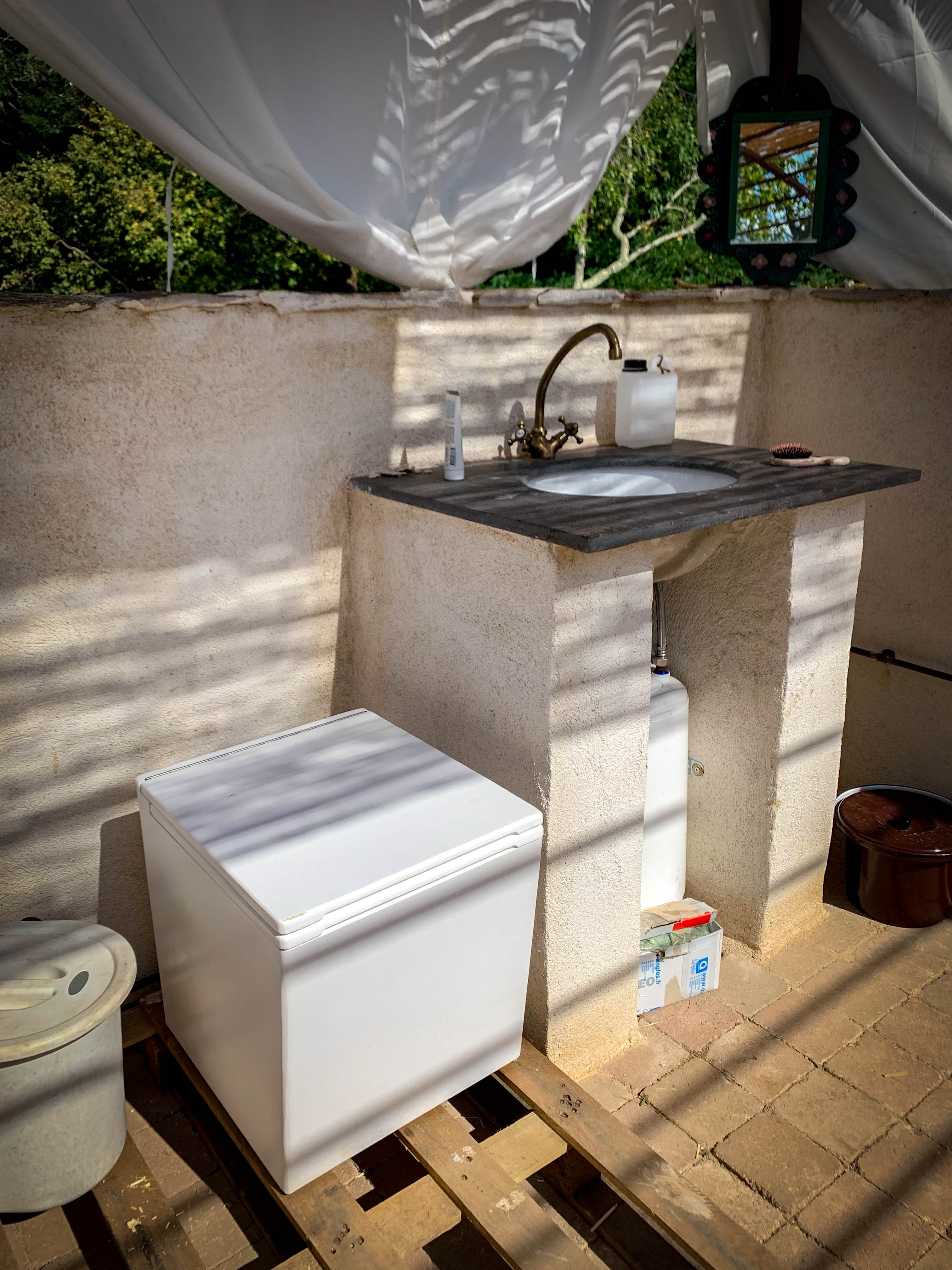 Outdoor bathroom with toilet and stone vanity with dappled sunlight